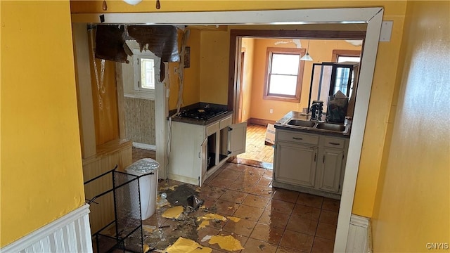 kitchen featuring plenty of natural light, black gas stovetop, a wainscoted wall, and a sink