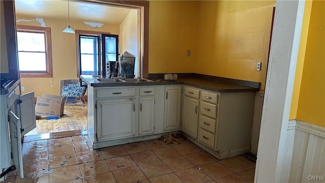 kitchen featuring dark countertops, wainscoting, hanging light fixtures, white cabinetry, and a sink