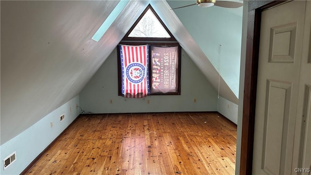 additional living space with visible vents, vaulted ceiling with skylight, hardwood / wood-style floors, and a ceiling fan