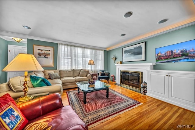 living area featuring a fireplace with flush hearth, wood finished floors, and ornamental molding