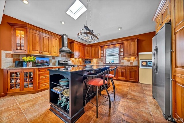 kitchen featuring tasteful backsplash, appliances with stainless steel finishes, brown cabinetry, and wall chimney range hood