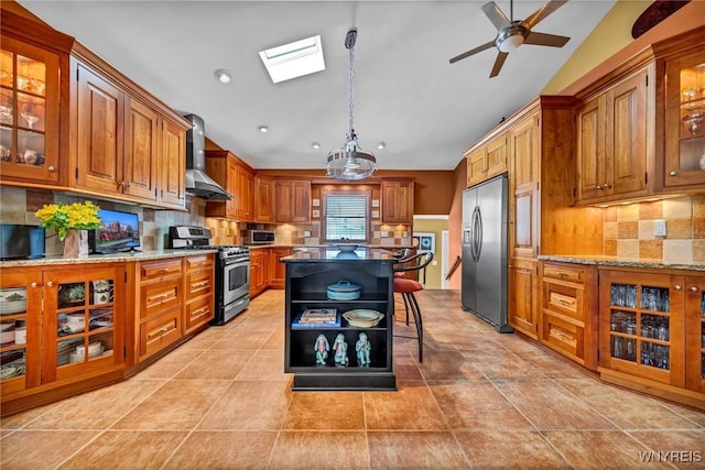 kitchen with wall chimney range hood, light stone countertops, lofted ceiling, brown cabinetry, and stainless steel appliances