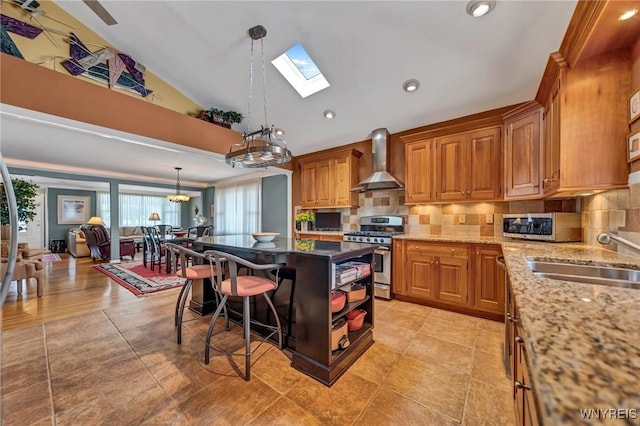 kitchen featuring a sink, stainless steel appliances, brown cabinets, and wall chimney range hood