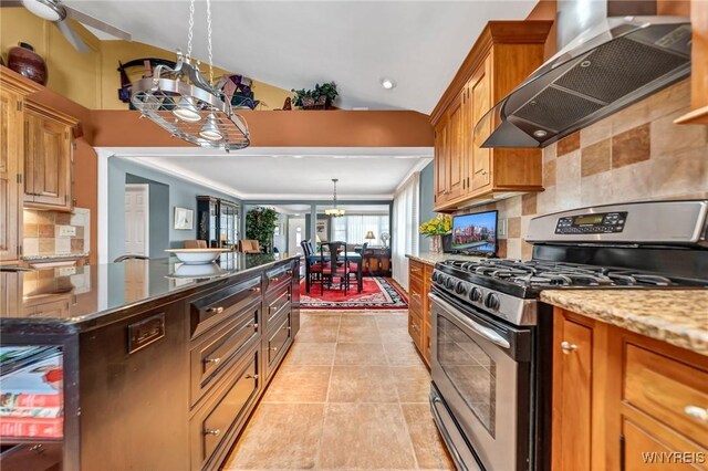 kitchen with wall chimney range hood, light tile patterned floors, brown cabinetry, and stainless steel gas range