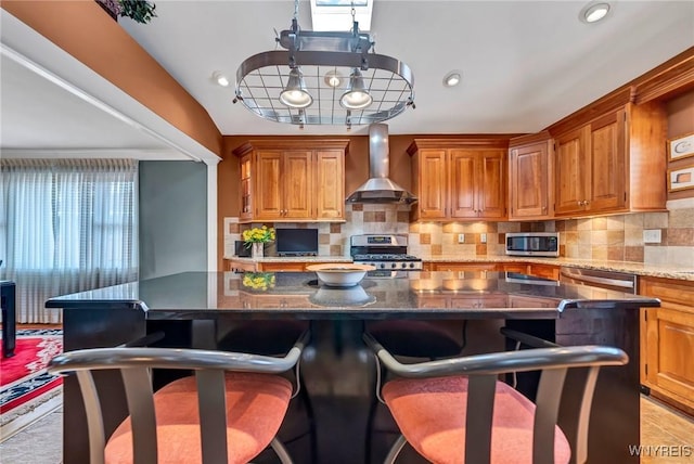 kitchen featuring stainless steel appliances, a kitchen bar, tasteful backsplash, and wall chimney range hood