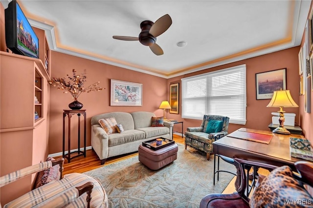 living area with baseboards, a ceiling fan, wood finished floors, and crown molding