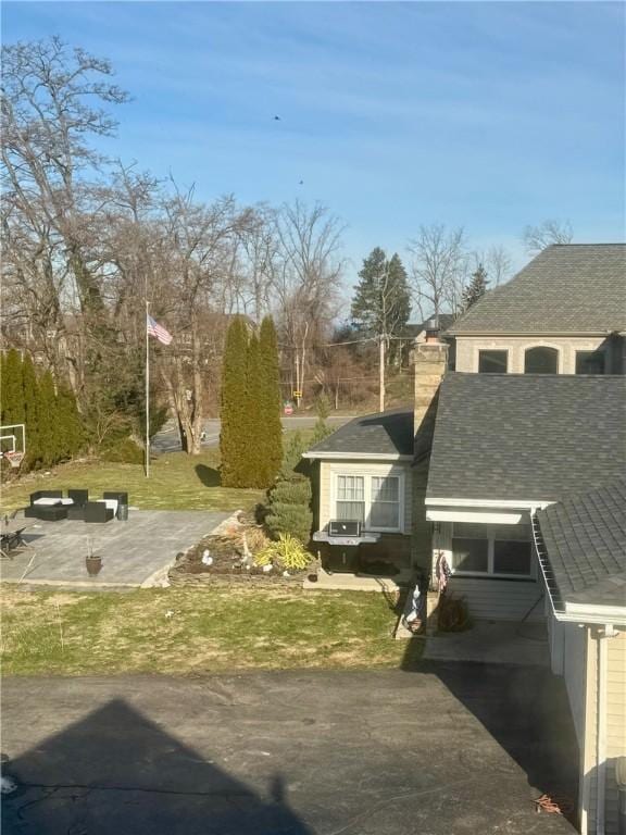 view of property exterior featuring a patio, a chimney, and a shingled roof