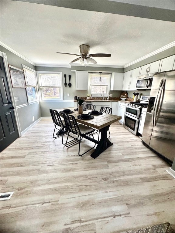 dining space featuring a textured ceiling, a ceiling fan, light wood-type flooring, and ornamental molding