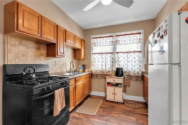 kitchen featuring freestanding refrigerator, a sink, decorative backsplash, dark wood-type flooring, and black range with gas cooktop