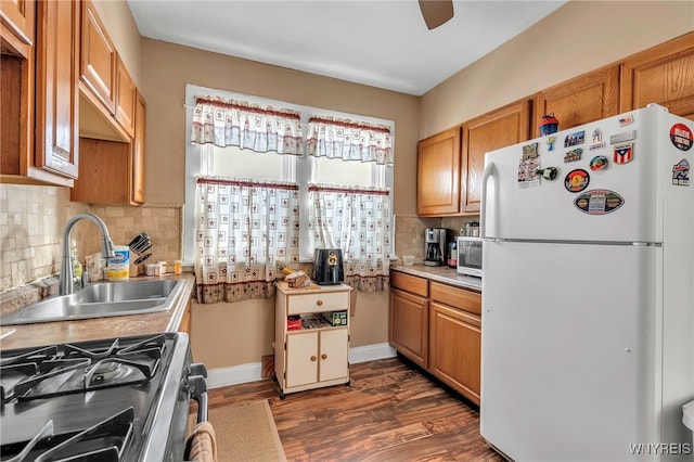 kitchen with a sink, decorative backsplash, brown cabinets, stainless steel appliances, and dark wood-style flooring