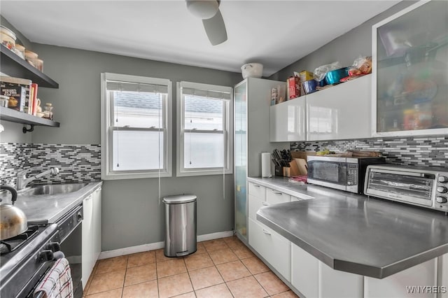 kitchen with light tile patterned floors, a sink, stainless steel counters, white cabinetry, and stainless steel microwave