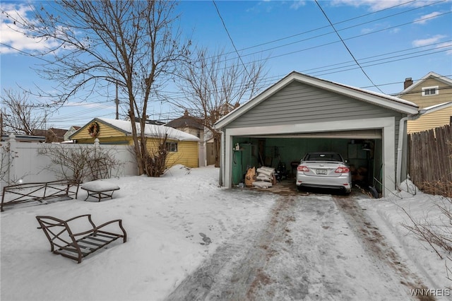 snow covered garage featuring a garage and fence