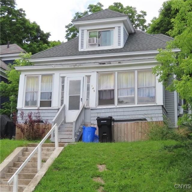 bungalow-style house with cooling unit, entry steps, a front lawn, and a shingled roof