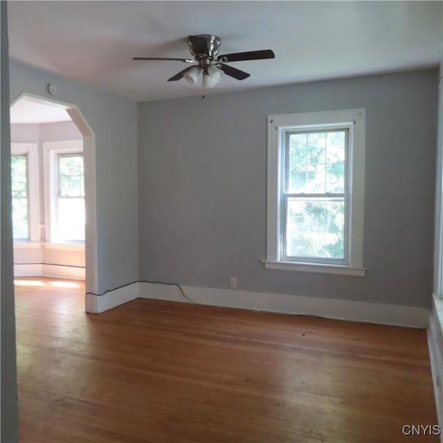 empty room with arched walkways, a ceiling fan, baseboards, and wood finished floors