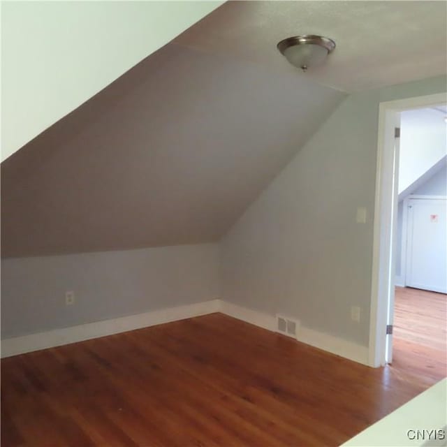 additional living space featuring vaulted ceiling, visible vents, baseboards, and wood finished floors