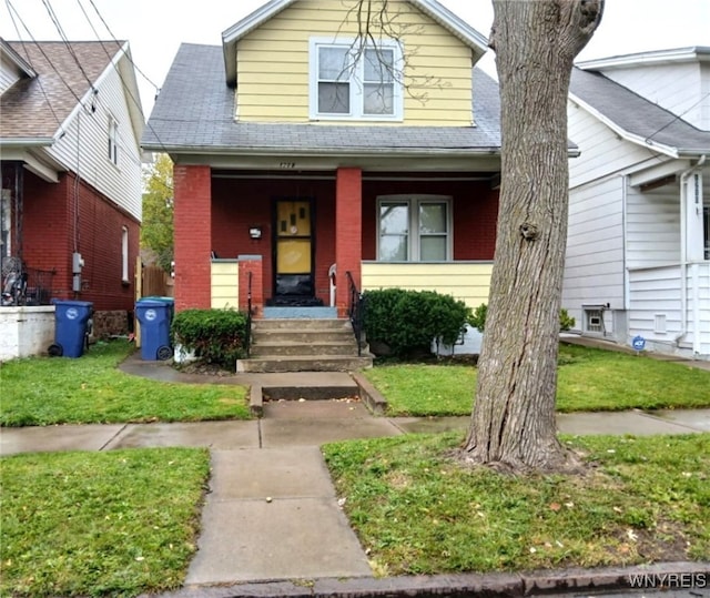 view of front of home with brick siding, a porch, a shingled roof, and a front yard