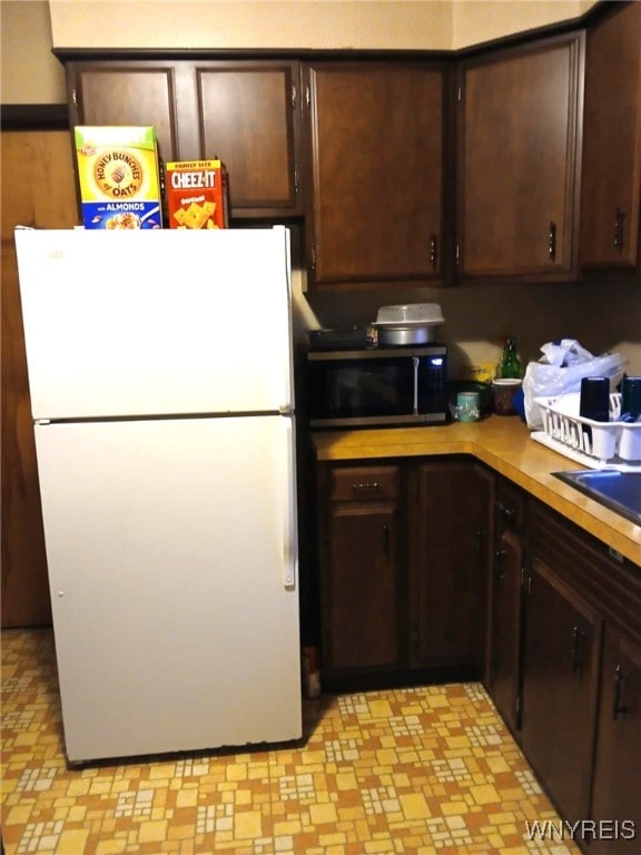 kitchen with stainless steel microwave, dark brown cabinets, light countertops, and freestanding refrigerator