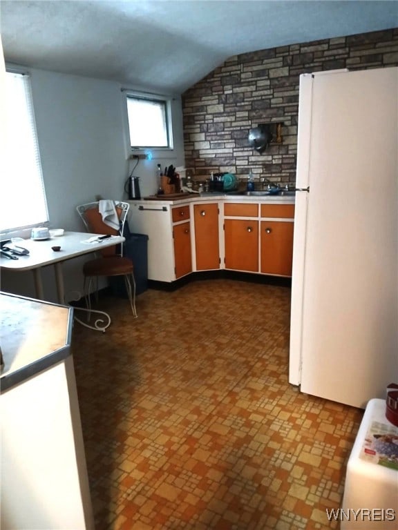 kitchen featuring dishwashing machine, light countertops, freestanding refrigerator, and lofted ceiling