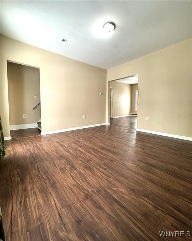 empty room featuring baseboards, dark wood-type flooring, and stairs