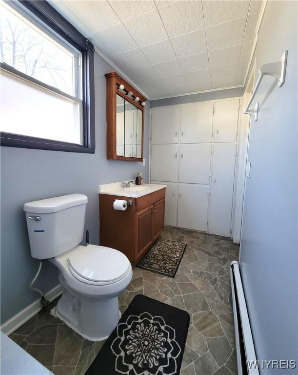 bathroom featuring toilet, stone finish floor, baseboards, baseboard heating, and vanity