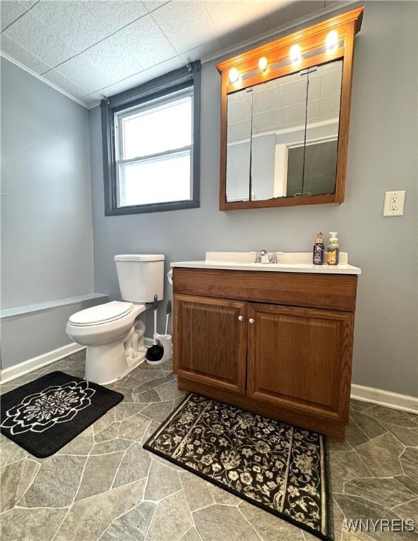 bathroom featuring toilet, a washtub, stone finish floor, baseboards, and vanity