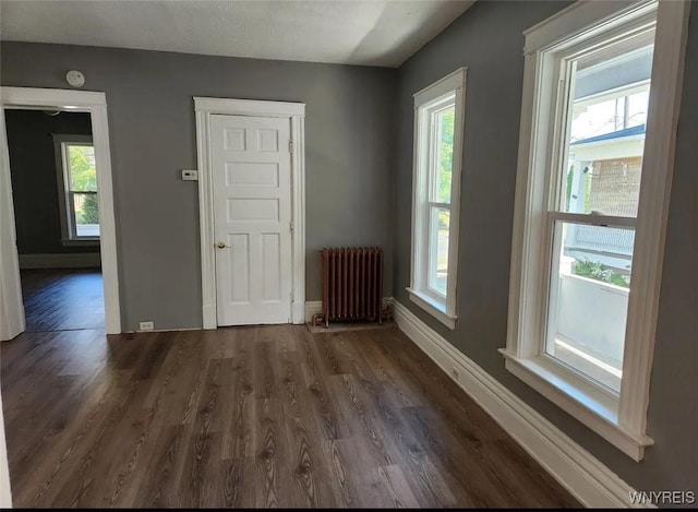 empty room featuring baseboards, plenty of natural light, dark wood-type flooring, and radiator heating unit