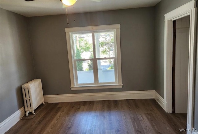 empty room with dark wood-style floors, a ceiling fan, radiator heating unit, and baseboards