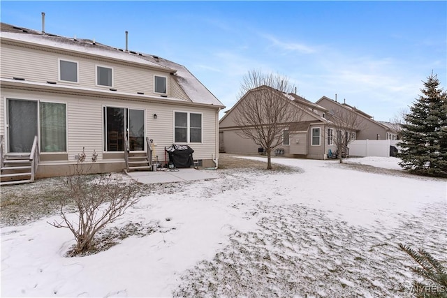 snow covered rear of property featuring entry steps, a garage, and fence