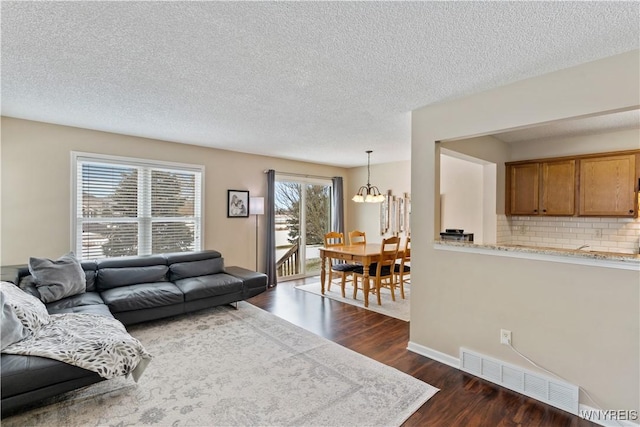 living area with visible vents, dark wood-type flooring, a notable chandelier, a textured ceiling, and baseboards