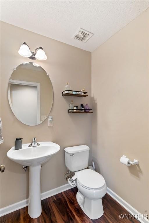 half bathroom featuring visible vents, baseboards, toilet, and wood finished floors