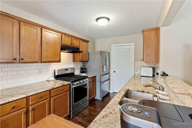 kitchen with under cabinet range hood, a sink, dark wood finished floors, appliances with stainless steel finishes, and brown cabinetry