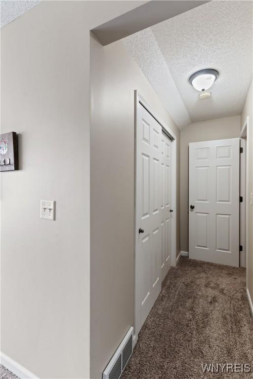 hall featuring visible vents, lofted ceiling, a textured ceiling, and carpet flooring