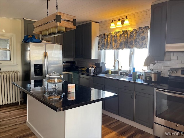 kitchen featuring dark countertops, backsplash, radiator, appliances with stainless steel finishes, and a sink