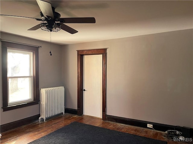 spare room with baseboards, radiator heating unit, dark wood-type flooring, and a ceiling fan