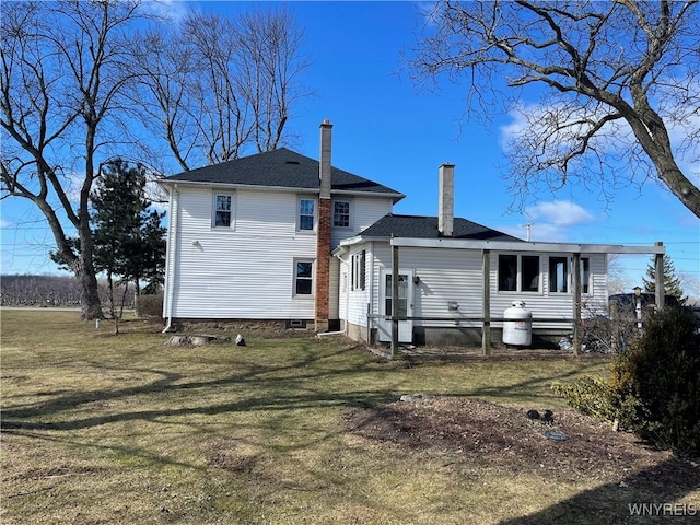 rear view of house with a chimney, a yard, and roof with shingles