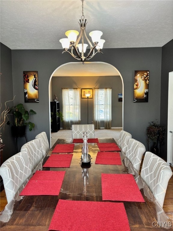 dining space featuring a textured ceiling, wood finished floors, arched walkways, an inviting chandelier, and baseboards