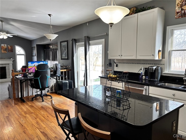 kitchen with a tiled fireplace, pendant lighting, light wood-style floors, white cabinetry, and a sink