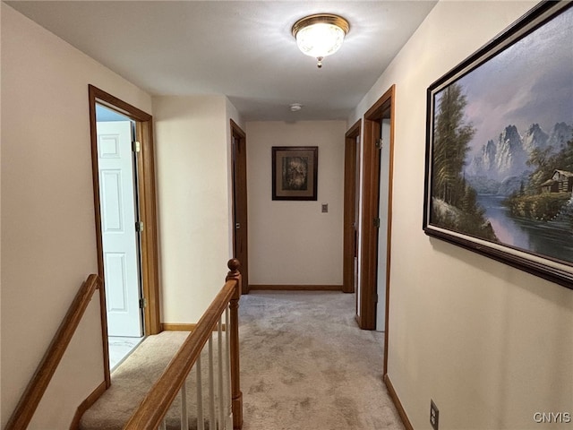 hallway featuring baseboards, an upstairs landing, and light carpet