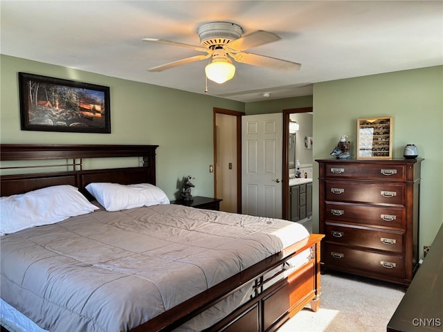 bedroom with a ceiling fan, light colored carpet, and connected bathroom