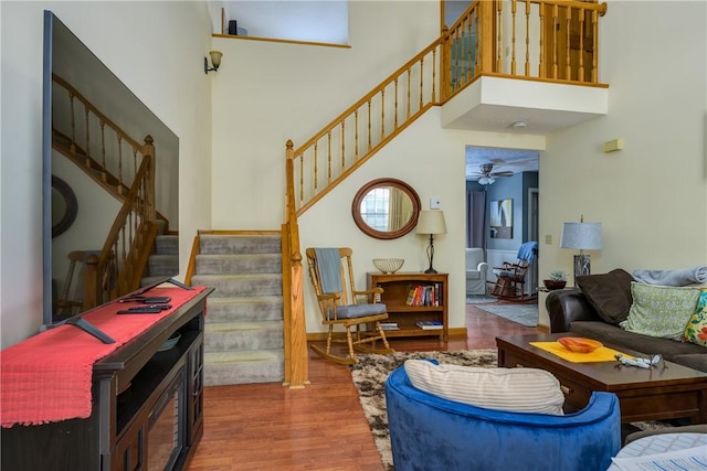 living area with stairway, wood finished floors, a high ceiling, and ceiling fan