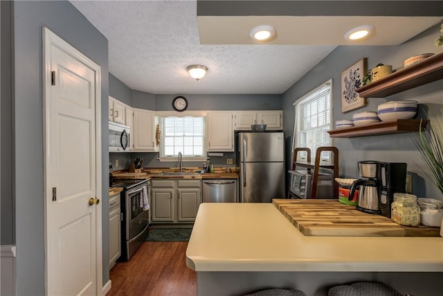 kitchen with dark wood-style flooring, a sink, stainless steel appliances, a textured ceiling, and white cabinetry