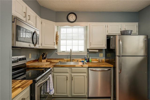 kitchen featuring a sink, a textured ceiling, appliances with stainless steel finishes, white cabinets, and wooden counters