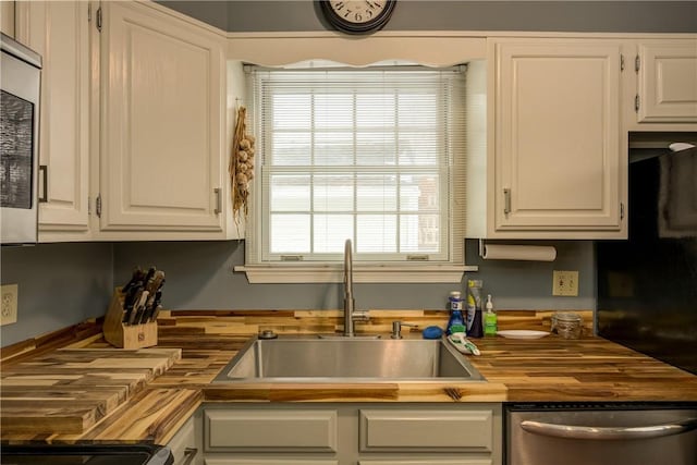 kitchen with butcher block counters, white cabinetry, dishwasher, and a sink