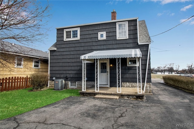 view of front of property featuring central air condition unit, a front lawn, a porch, fence, and a chimney