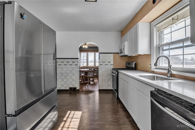 kitchen featuring dark wood finished floors, light countertops, appliances with stainless steel finishes, arched walkways, and a sink