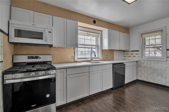 kitchen with dark wood finished floors, a sink, decorative backsplash, light countertops, and appliances with stainless steel finishes