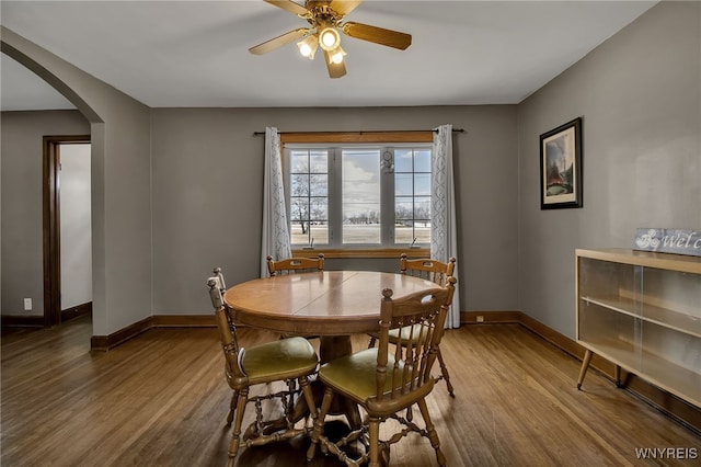 dining room with ceiling fan, baseboards, arched walkways, and wood finished floors