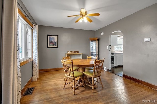 dining space with wood finished floors, plenty of natural light, arched walkways, and visible vents