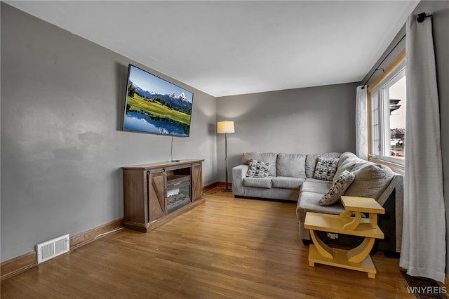 living area featuring a fireplace, wood finished floors, visible vents, and baseboards