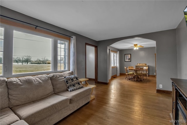 living room featuring arched walkways, baseboards, light wood-style floors, and a ceiling fan